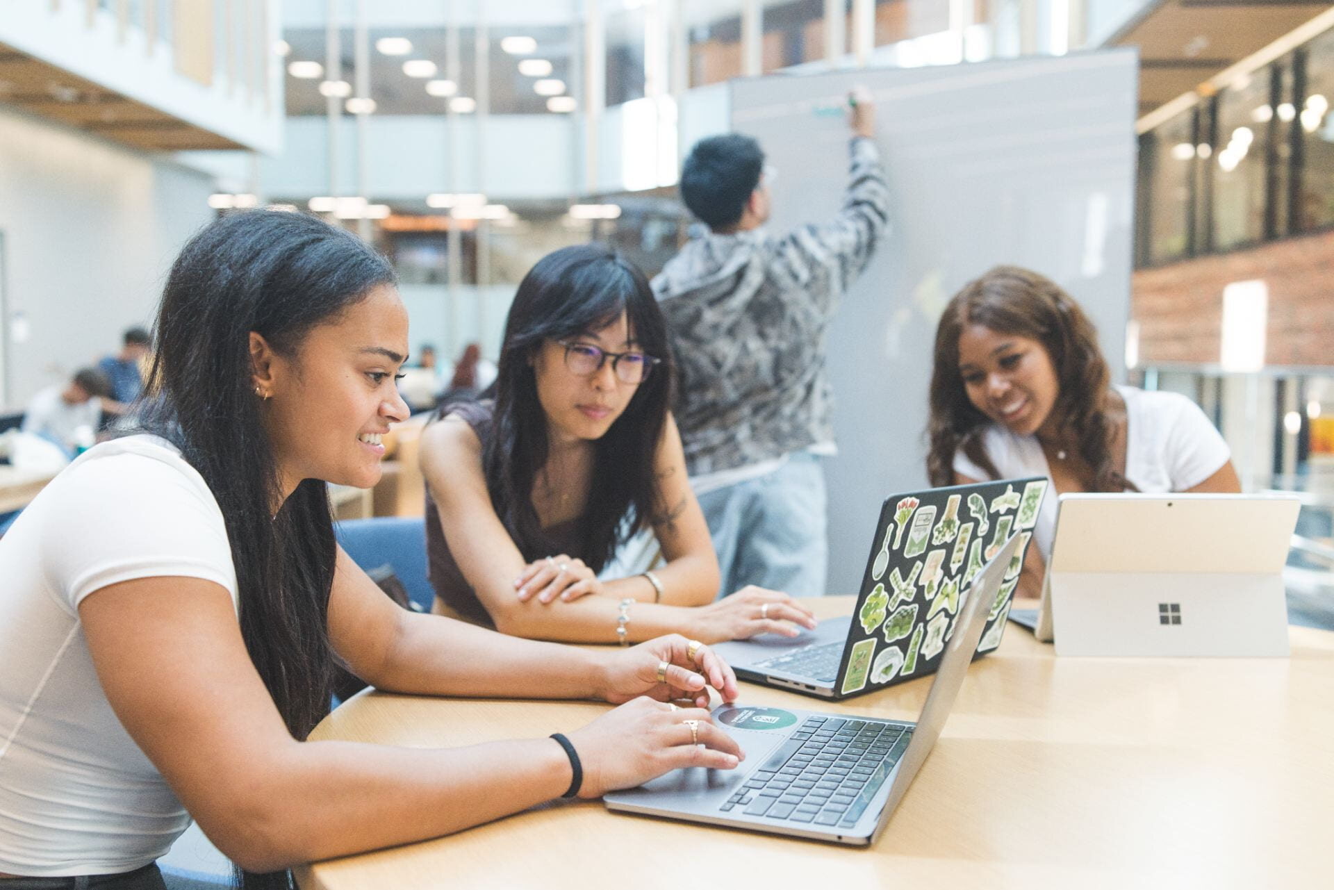 Dartmouth students working together on laptops while a teammate writes on a whiteboard behind them