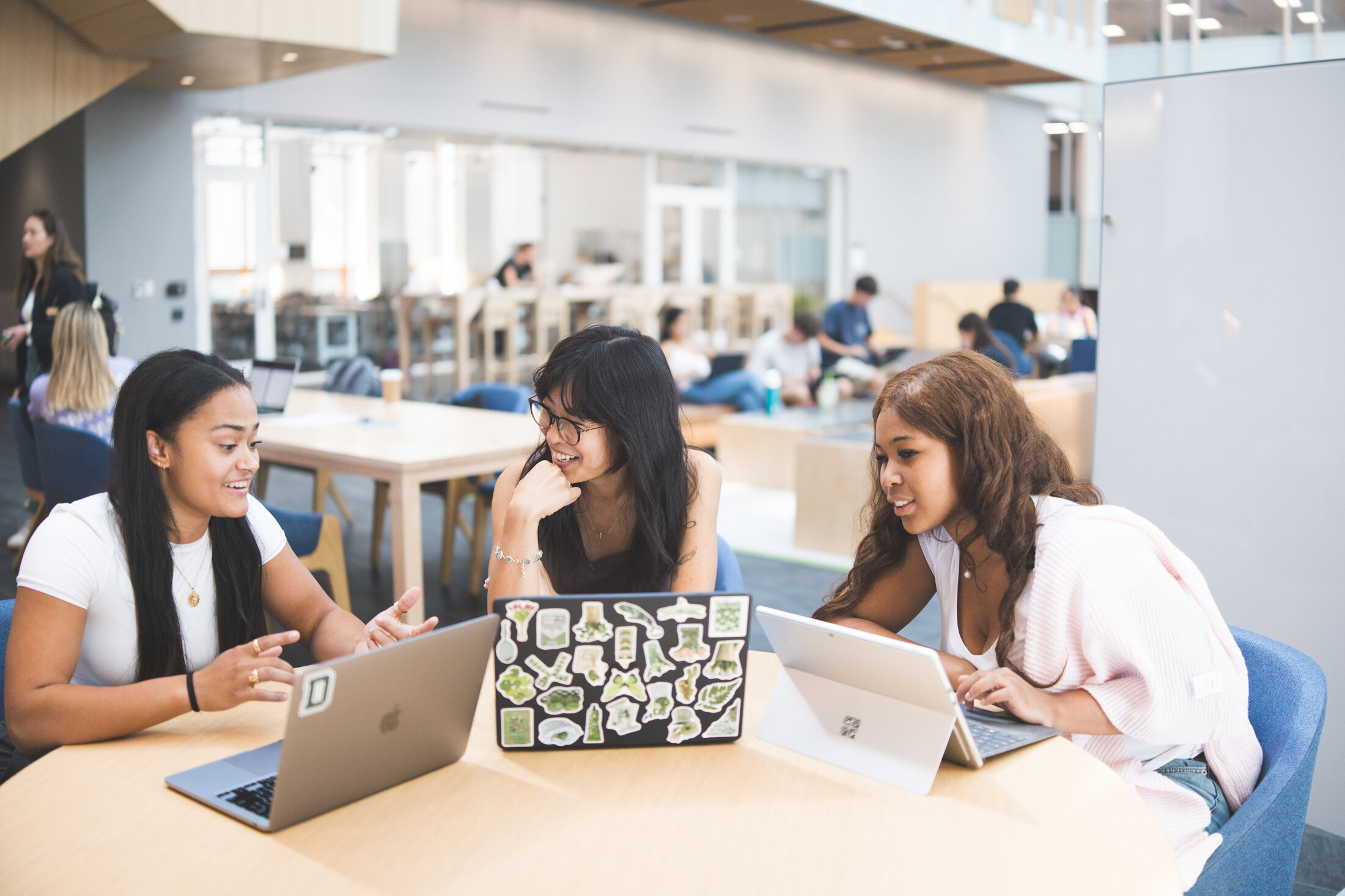 Three Evergreen students smiling around sticker-covered laptops during a working session