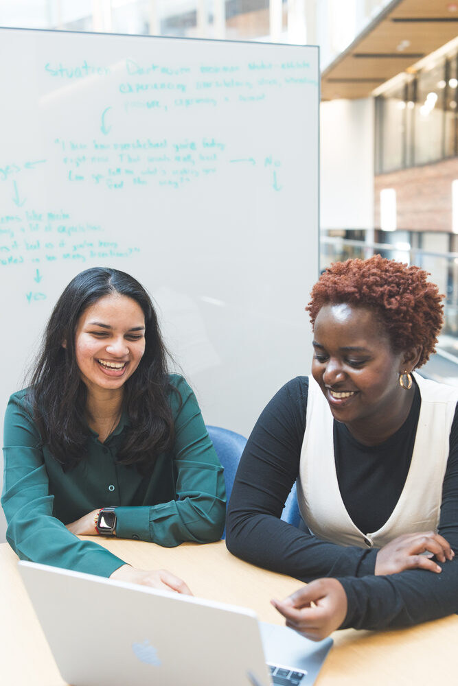 Two students laughing together during a working session at a whiteboard